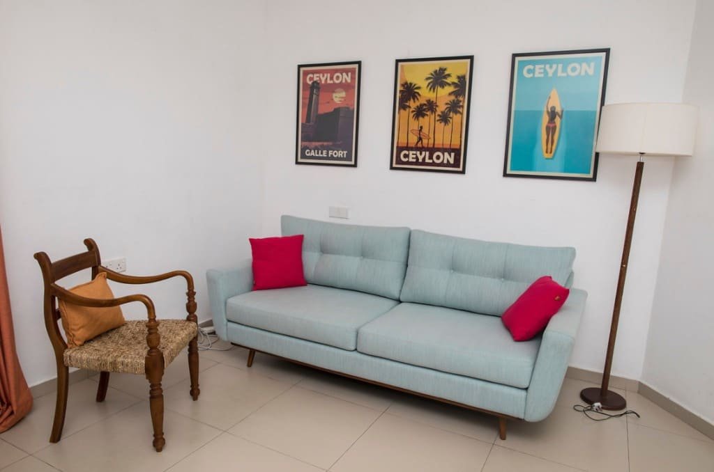 A lounge with a blue sofa, wooden armchair and Ceylon posters